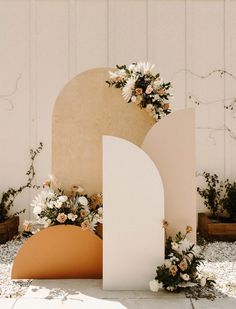 an arch with flowers on it is in front of a white wall and some plants