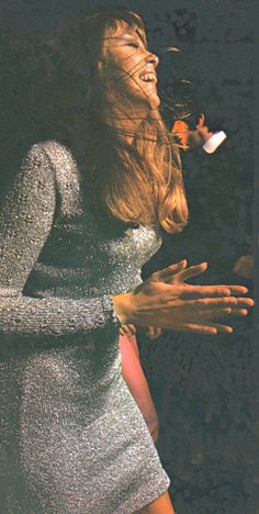 a woman in a silver dress singing into a microphone with her hands out to the side