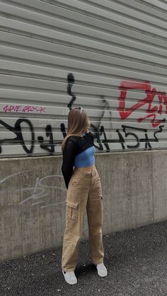 a woman standing in front of a wall with graffiti on it and her back to the camera