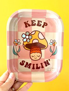 a person holding up a pink and white tray with a mushroom on it that says keep smiling