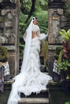 a woman in a white wedding dress and veil is standing on some steps with her back to the camera