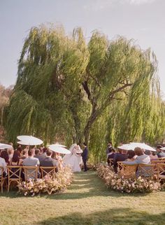 an outdoor wedding ceremony with white umbrellas and flowers on the grass, under a willow tree