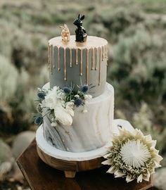 a three tiered cake with frosting dripping down the side and flowers on top