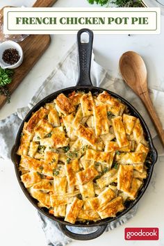 a skillet filled with chicken pot pie on top of a white table next to wooden spoons