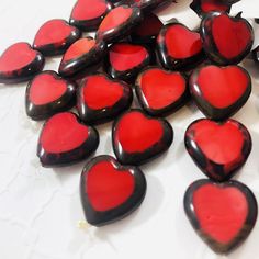 red and black heart shaped glass cabochons on a white counter top with other hearts in the background