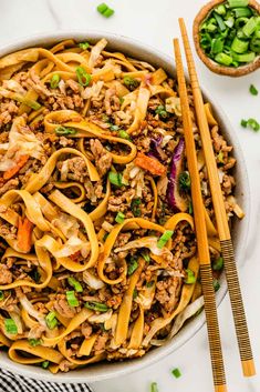 a bowl filled with noodles, meat and vegetables next to chopsticks on the side