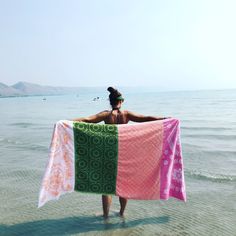 a woman standing in the water with a towel on her back, holding up an ocean view