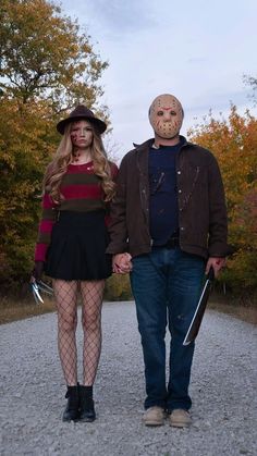 a man and woman dressed up as zombies walking down a gravel road with trees in the background