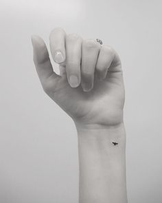 a woman's hand with a tiny black bird tattoo on it, holding up her thumb