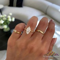 a woman's hand with two rings on it and a flower vase in the background