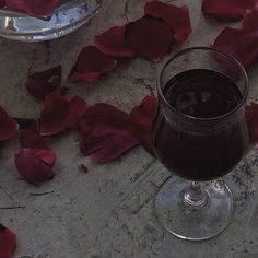 a glass filled with liquid sitting on top of a table next to red rose petals