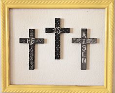 three wooden crosses mounted to a wall in a yellow frame with the word jesus written on it