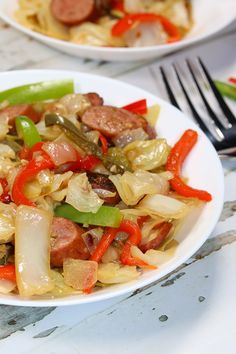 a white plate topped with sausage and peppers next to a fork on top of a table