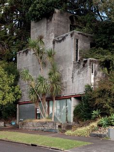 an old concrete building with palm trees in the foreground and bushes on the other side