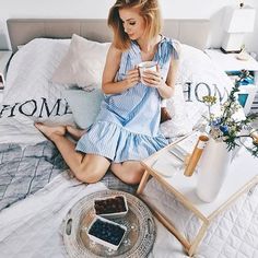 a woman sitting on a bed looking at her cell phone and holding a cup in one hand