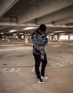 a man standing in an empty parking lot looking at his cell phone while wearing black and white sneakers