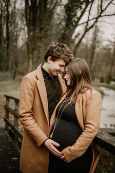 a pregnant couple standing next to each other on a bridge