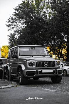 a mercedes g - class is parked in a parking lot next to other cars and trees