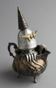 an old fashioned teapot with a key in it's mouth and a metal cup on the side