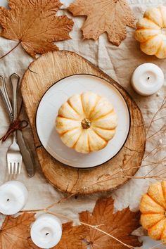 a white plate topped with a pumpkin on top of a wooden table next to candles