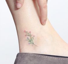 a small flower tattoo on the ankle that is being held up by someone's hand