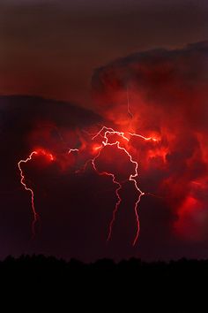 the sky is filled with bright red clouds as lightning strikes in the distance behind it