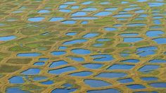 an aerial view of water and land with patches of grass in the foreground, taken from above