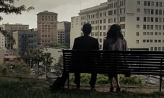 two people sitting on a bench looking at the city