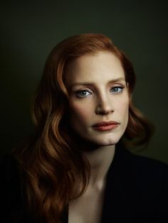 a woman with red hair and blue eyes looks into the camera while wearing a black jacket