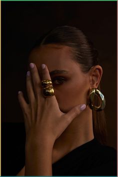 a woman holding her hands to her face with two rings around her neck and one hand on the other side of her face