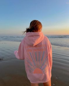 a woman is walking on the beach wearing a pink hoodie that says let watch the sunset