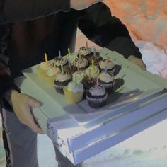 a person holding a box with cupcakes on it in front of other people