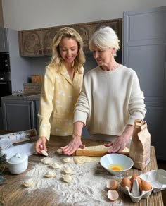 two women in the kitchen preparing food on a wooden table with flour, eggs and bread