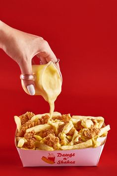 a person pouring sauce over some food in a container on a red tableclothed surface