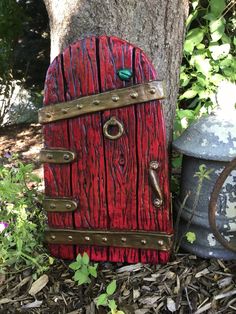 a red and brown fairy door sitting next to a potted planter on the ground