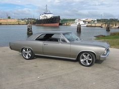 an old car parked in front of a large boat