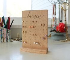 a wooden peg board with several pairs of earrings on it and a pen holder in the background