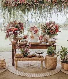 an arrangement of flowers and plants on display under a wooden structure with wicker baskets