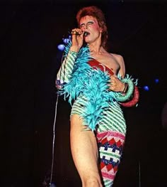 a woman in a costume singing into a microphone with feathers on her body and legs