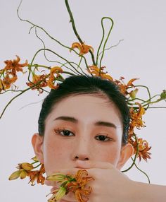 a woman with flowers in her hair covering her mouth and hand over her mouth, looking at the camera