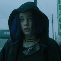 a woman with blue hair wearing a black hoodie and looking off to the side