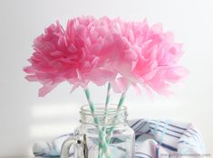 two pink flowers in a mason jar with straws on the table next to it