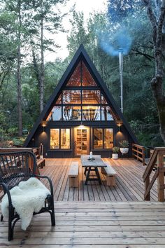 a - frame cabin in the woods with wooden decking and outdoor furniture on it