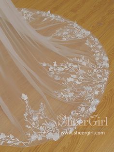 a wedding veil with flowers and leaves on the bottom is laying on a wooden floor