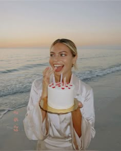 a woman holding a cake with candles in her mouth on the beach at sunset time