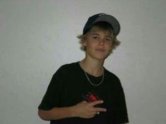 a young boy wearing a black shirt and a baseball cap standing in front of a white wall