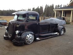 an old black truck parked in front of a house with a tarp on it's hood