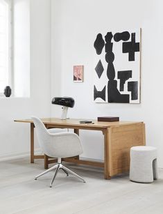 an office with a desk, chair and art on the wall above it in a white room