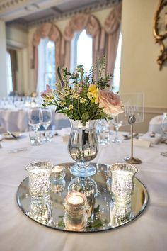 a vase with flowers and candles is sitting on a glass plate in the middle of a table