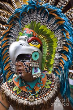 a man in an elaborate headdress with feathers on his head and face painted multicolored